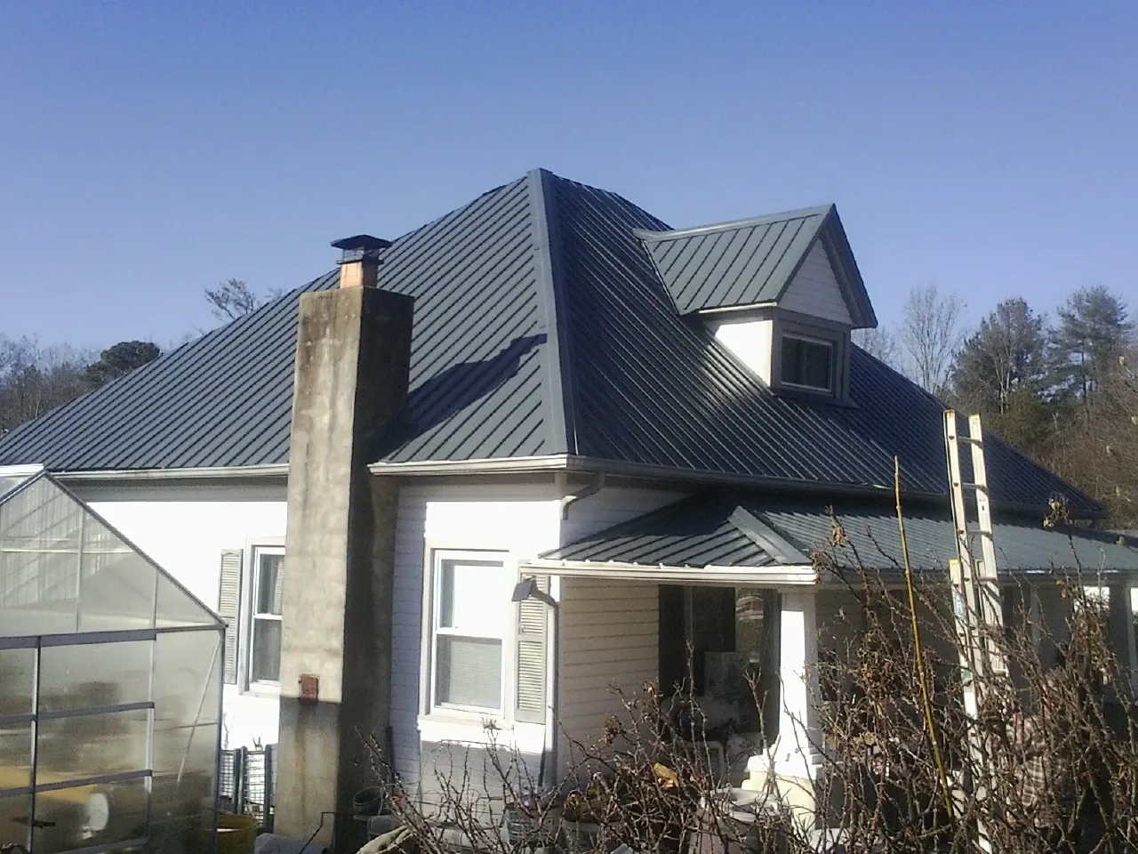 Dark blue standing seam metal roof on a white farmhouse with dormer — Slate & Tile Roof Repair by Roofing Brothers in Arimo