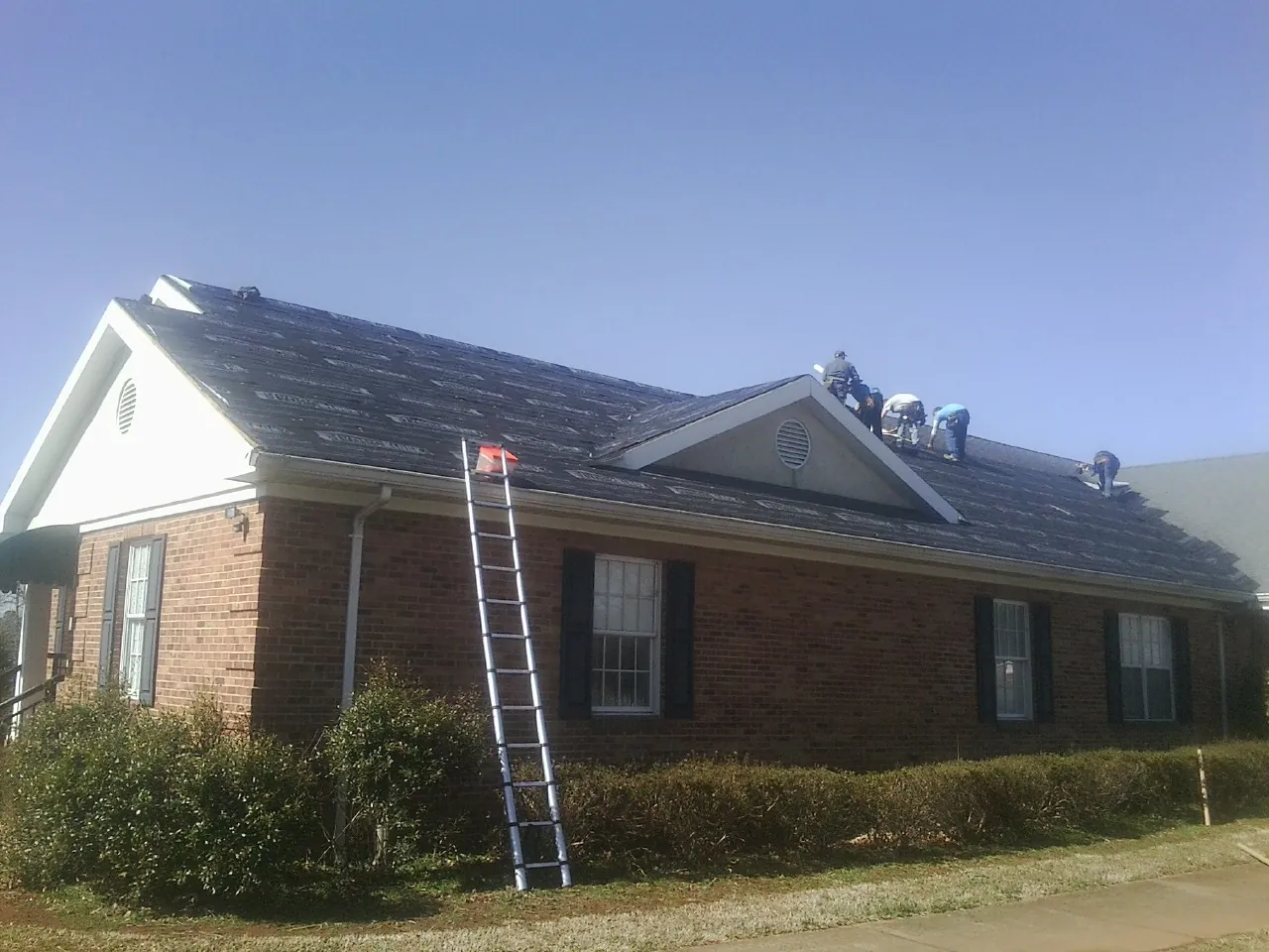 Crew tearing shingles off a brick ranch roof with a ladder set — Metal Roof Repair work by our crew in Arimo