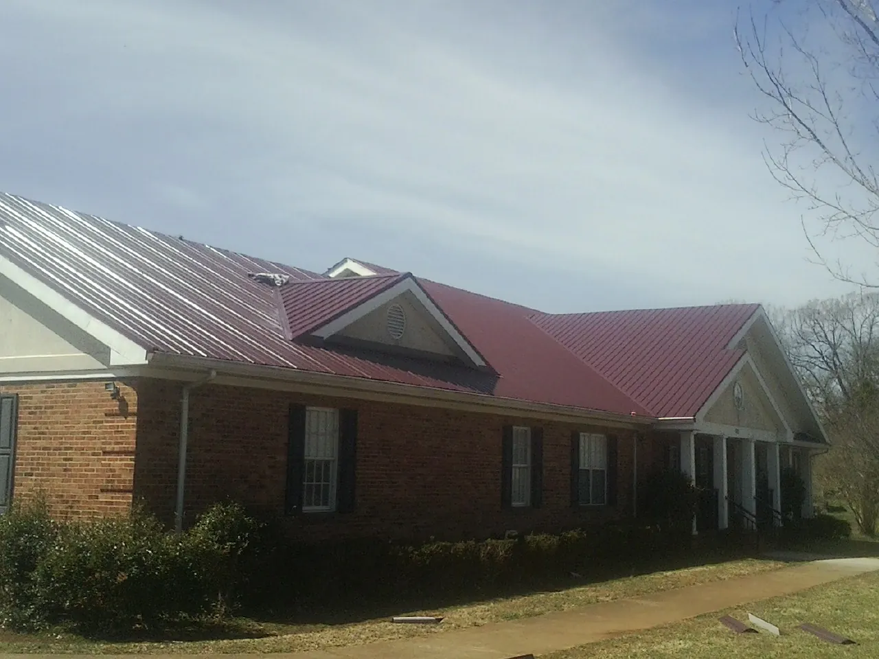 Red metal roof with gabled entries on a long brick building, from a Hail Damage Roof Repair job in Arimo