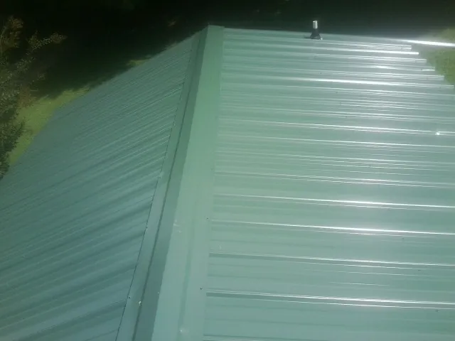 New green metal panels meeting at the ridge of a roof — Flat Roof Repair work by our crew in Arimo