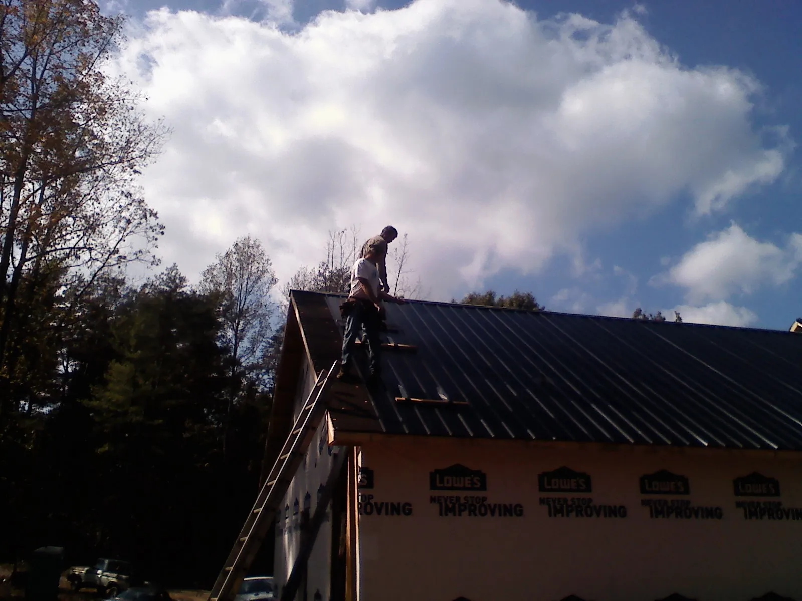 Roofer fastening dark metal panels high against a cloudy sky, from a Roof Inspection job in Arimo